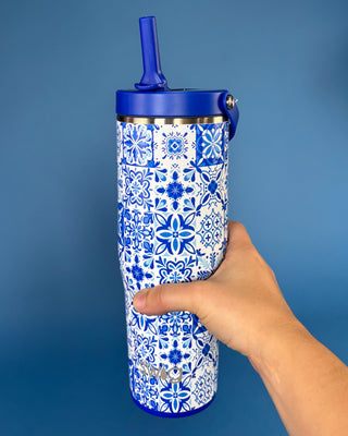 A hand holding a tall insulated tumbler with a blue and white floral tile pattern, blue lid