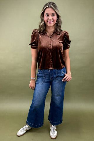 Woman wearing a brown blouse and blue jeans against a green background