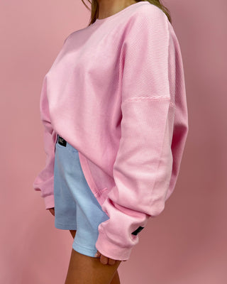 Person wearing a pink corduroy sweatshirt and light blue shorts on a pink background