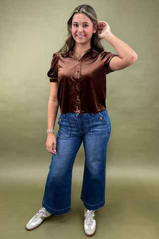 Woman wearing a brown blouse and blue jeans against a green background