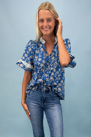 Woman wearing a blue floral blouse and jeans against a light blue background