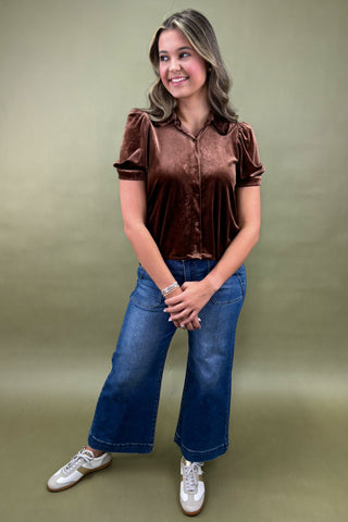 Woman wearing a brown velvet blouse and blue jeans against a green background