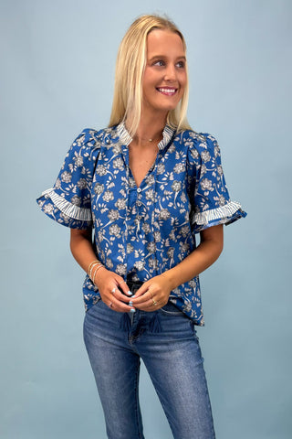 Woman wearing a blue floral blouse with ruffled sleeves against a light blue background