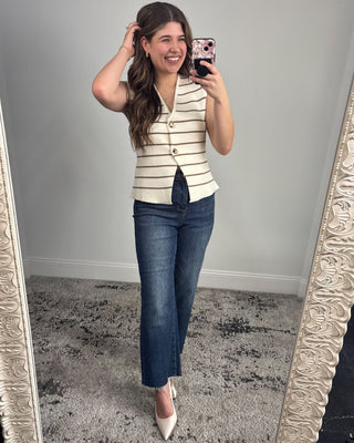 Woman taking a mirror selfie wearing a striped vest and blue jeans.