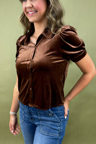 Woman wearing a brown velvet blouse and blue jeans against a green background