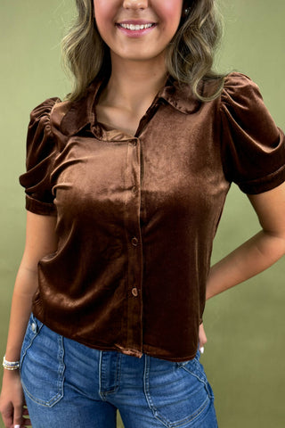 Woman wearing a brown velvet blouse and blue jeans against a green background