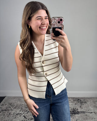 Woman taking a mirror selfie wearing a striped vest and jeans against a gray background