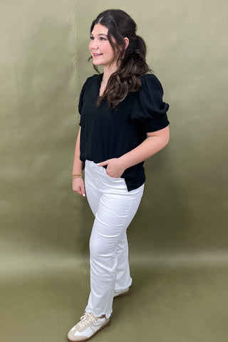 Woman wearing a black top and white pants against a green background