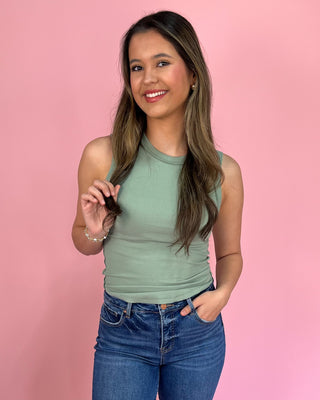 Woman wearing a green sleeveless top and blue jeans against a pink background