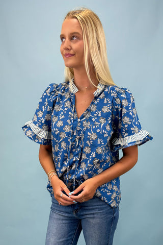 Woman wearing a blue floral blouse with white ruffled sleeves against a light blue background