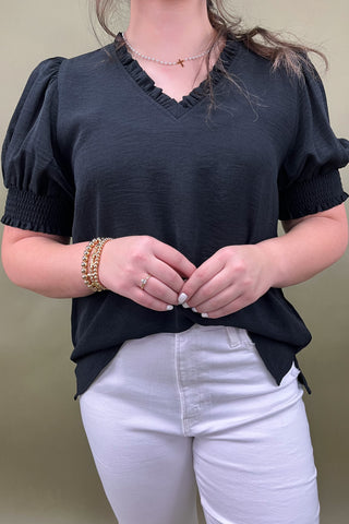 Person wearing a black top with puff sleeves and white pants against a beige background