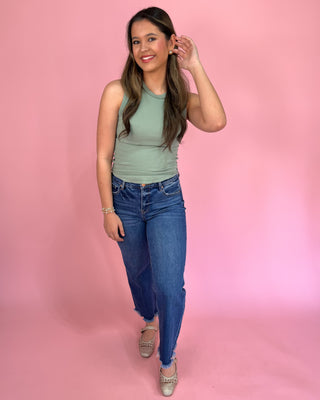 Woman wearing a green tank top and blue jeans against a pink background