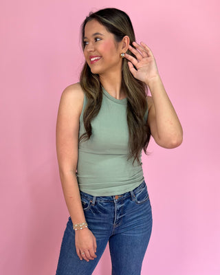 Woman wearing a green sleeveless top and blue jeans against a pink background