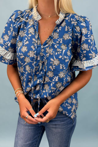 Woman wearing a blue floral blouse with ruffled sleeves against a light blue background
