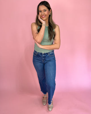 Woman wearing a green sleeveless top and blue jeans against a pink background