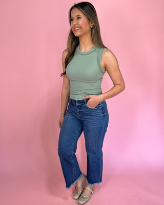 Woman wearing a green sleeveless top and blue jeans against a pink background