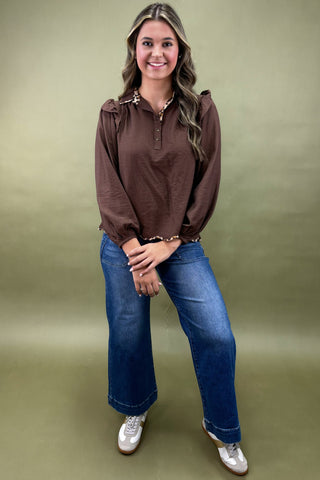 Woman wearing a brown blouse and blue jeans against a green background