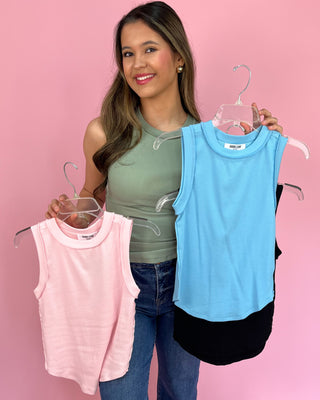 Woman holding two sleeveless tops, one pink and one blue, on a pink background