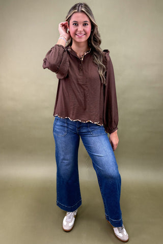 Woman wearing a brown blouse and blue jeans against a green background
