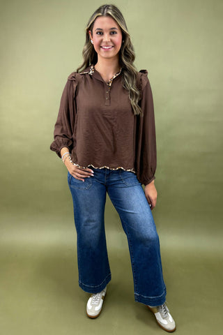 Woman wearing a brown blouse and blue jeans against a green background