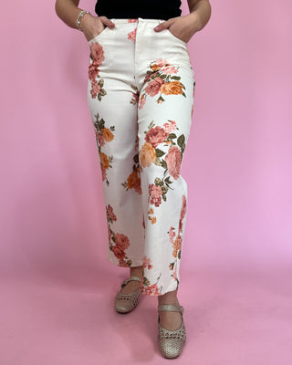 Person wearing white pants with floral pattern on a pink background