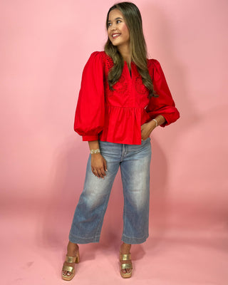 Woman wearing a red blouse and blue jeans against a pink background