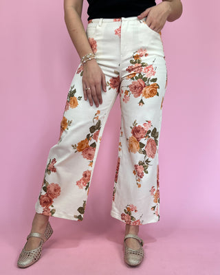 Person wearing white floral pants on a pink background