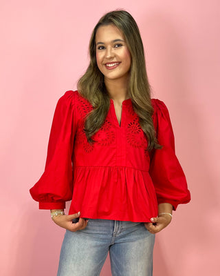 Woman wearing a red blouse with lace details against a pink background