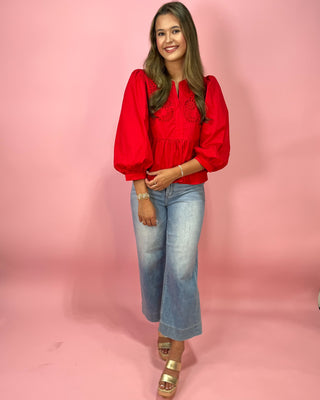 Woman wearing a red blouse and blue jeans against a pink background