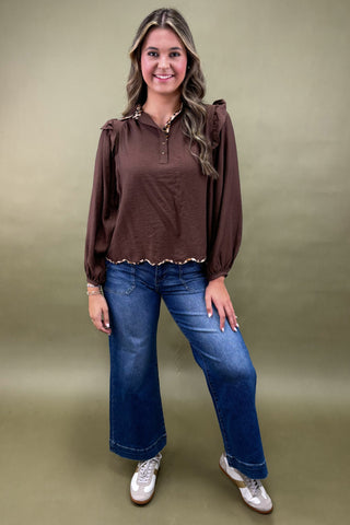 Woman wearing a brown blouse and blue jeans against a green background