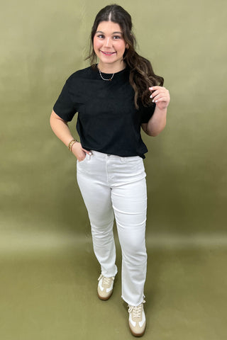 Woman wearing a black t-shirt, white jeans, and gold shoes against a green background