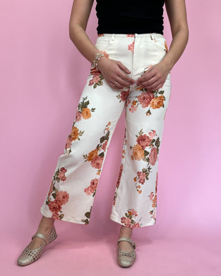 Person wearing white floral pants on a pink background