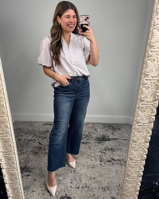 Woman taking a mirror selfie wearing a striped shirt and jeans, standing in front of an ornate mirror.