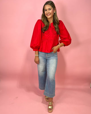 Woman wearing a red blouse and blue jeans against a pink background