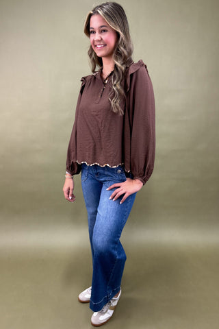 Woman wearing a brown blouse and blue jeans against a beige background