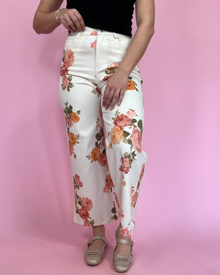 Person wearing white floral pants on a pink background