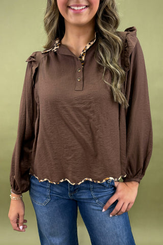 Woman wearing a brown blouse with ruffled details and blue jeans on a green background