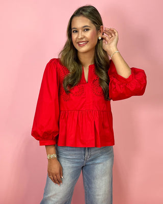 Woman wearing a red blouse with embroidery and light blue jeans on a pink background
