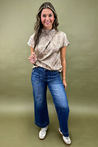 Woman wearing a patterned top and blue jeans against an olive green background