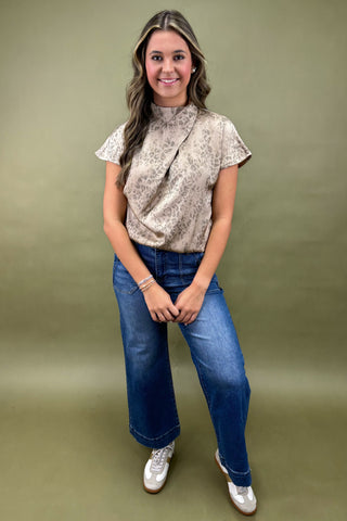 Woman wearing a patterned blouse and blue jeans against a green background