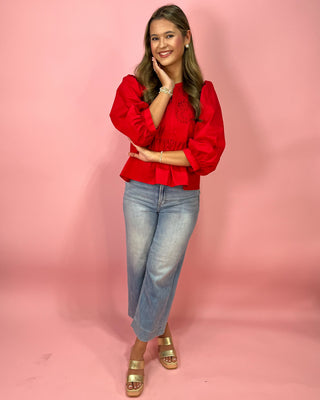 Woman wearing a red blouse and blue jeans against a pink background