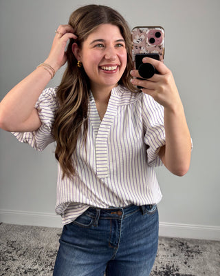 Woman taking a mirror selfie wearing a striped shirt and jeans against a plain background