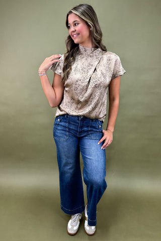 Woman wearing a patterned blouse and blue jeans against a green background
