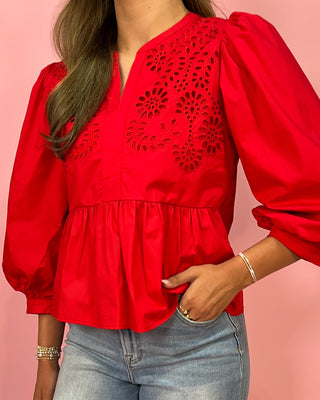 Red blouse with intricate cut-out design worn by a person on a pink background