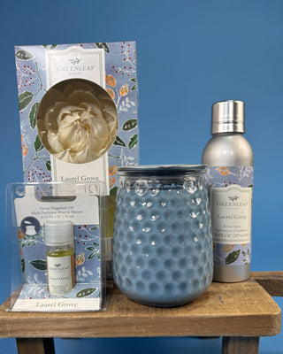 Greenleaf Candle Co. Laurel Grove home fragrance set displayed on a wooden shelf against a blue background, including a large blue textured jar candle, a silver bottle, a small oil bottle in a clear package, and the branded box.