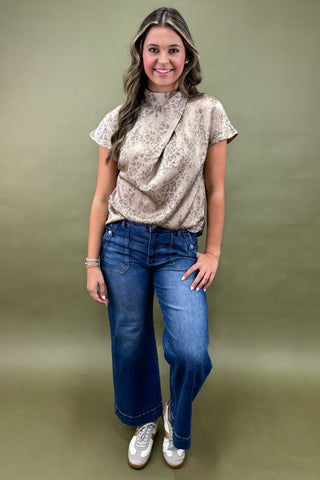 Woman wearing a patterned top and blue jeans against a green background