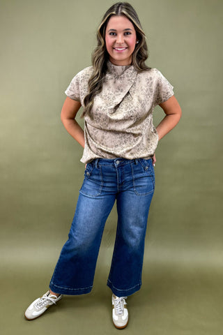 Woman wearing a patterned top and blue jeans against a green background
