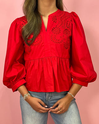 Red blouse with intricate detailing worn by a person on a pink background