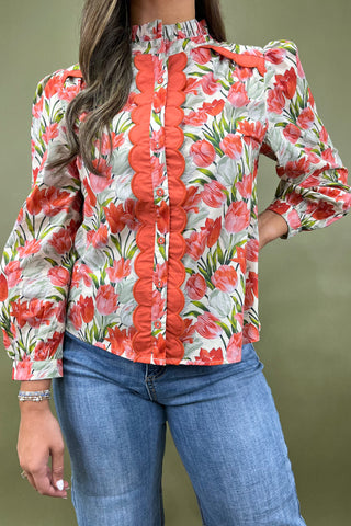 Woman wearing a floral blouse with red flowers and blue jeans on a plain background