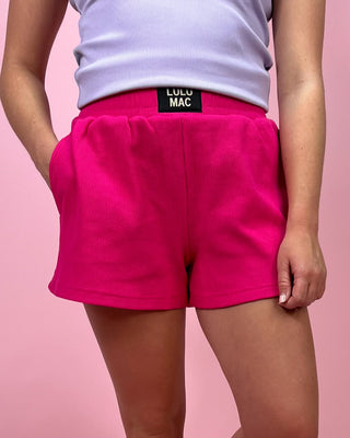 Person wearing bright pink shorts with a visible brand label on a pink background